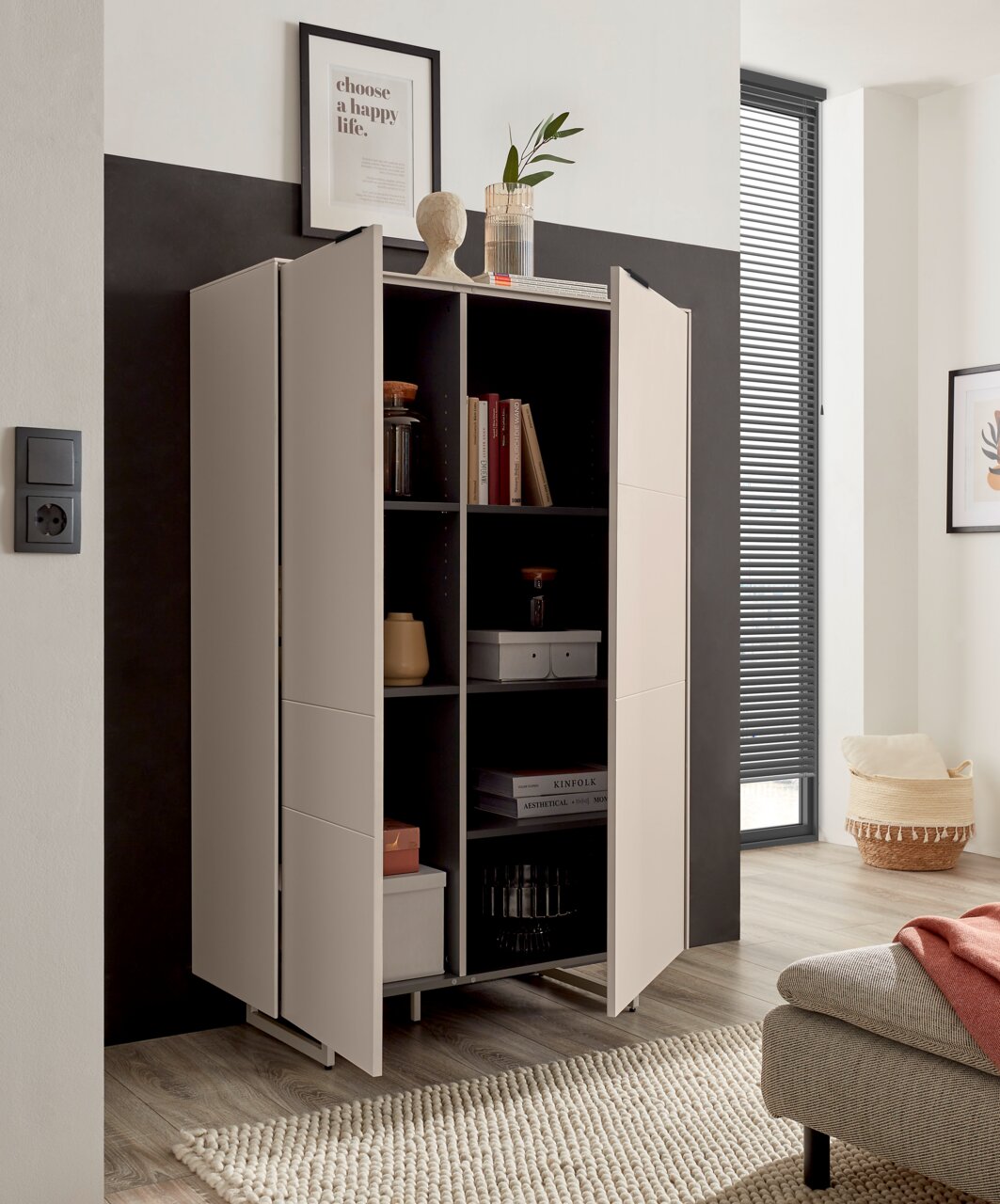 Modern, lichtgrijs hoogkast/kast met twee open deuren en zwarte binnenvakken, versierd met boeken en accessoires, in een woonkamer – vooraanzicht vanuit een licht schuin perspectief van links.