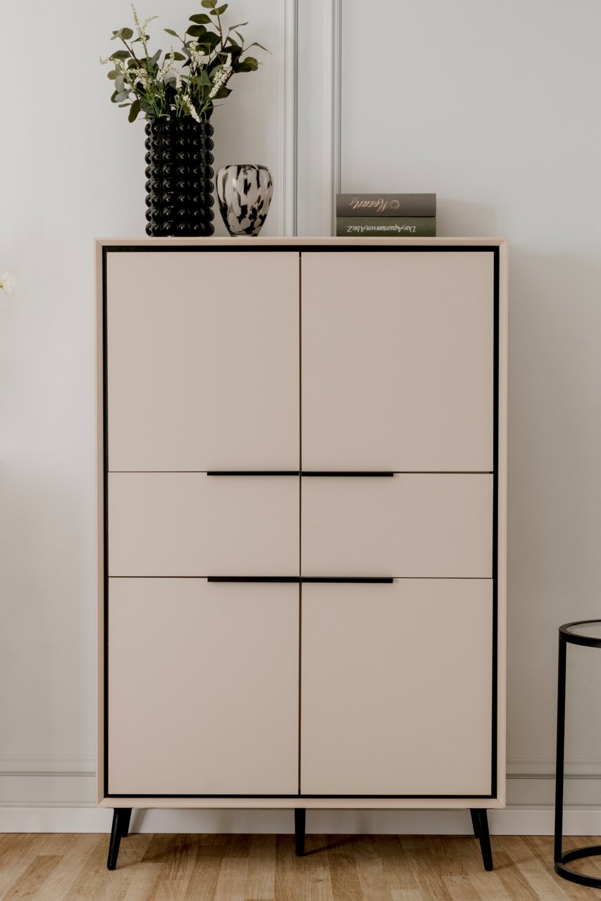 Modernes Highboard mit vier Türen, schwarzem Rahmen und Beinen, dekoriert mit einer Vase und einem Buch, Frontalansicht.