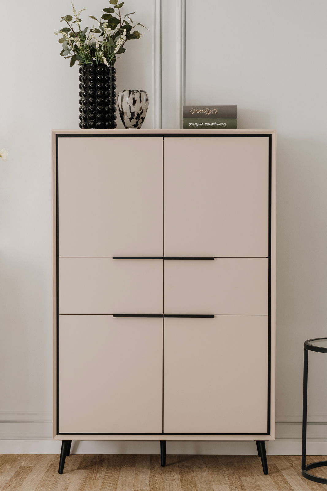 Modernes Highboard mit vier Türen, schwarzem Rahmen und Beinen, dekoriert mit einer Vase und einem Buch, Frontalansicht.