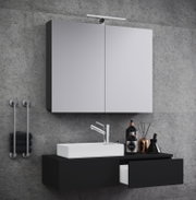 Modernes Badezimmer-Set mit beleuchtetem Spiegelschrank, weißem Aufsatzwaschbecken und schwarzem Waschtischunterschrank vor Betonwand, perspektivisch in leichter Seitenansicht von vorn
