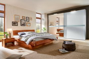Modernes Schlafzimmer mit einem eleganten Holzbett und einem großen Kleiderschrank mit Schiebetüren, seitliche Perspektive.
