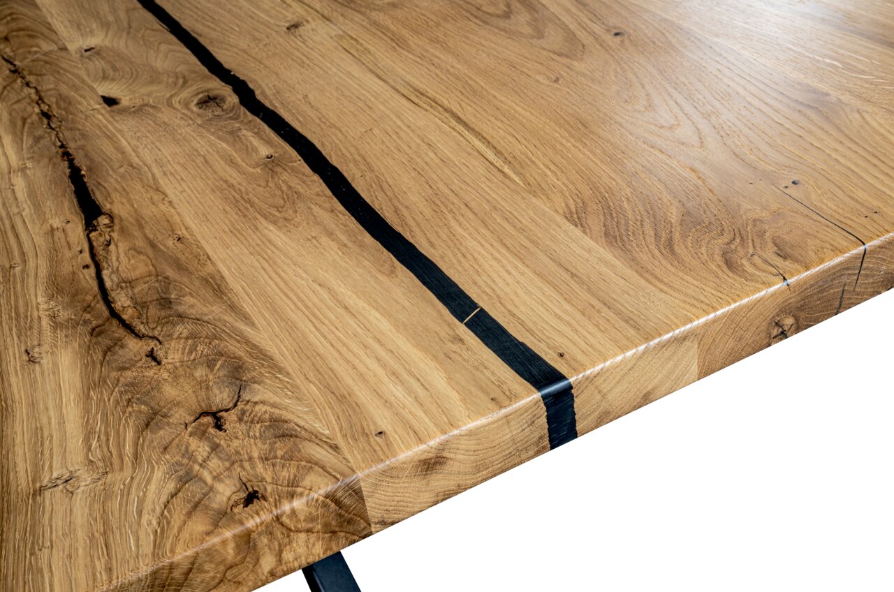 Nahaufnahme eines Esstisches aus Holz mit natürlicher Maserung und schwarzen Akzenten, Perspektive von oben.