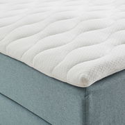 Nahaufnahme eines Boxspringbetts mit weißem, gestepptem Topper und hellblauem Stoffbezug, seitliche Perspektive