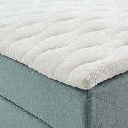 Nahaufnahme eines Boxspringbetts mit weißem, gestepptem Topper und hellblauem Stoffbezug, seitliche Perspektive