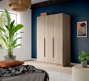 Heller 3-türiger Kleiderschrank in Holzoptik mit langen schwarzen Griffen, im Schlafzimmer vor dunkelblauer Wand, Perspektive: frontale Ansicht leicht von links