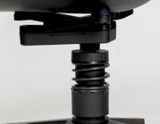 Close-up zijaanzicht van een zwarte gasveer met verstelring en mechanisme onder een bureaustoelzitting op een witte achtergrond