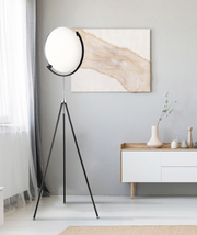 Moderne LED-Stehleuchte mit rundem, weißem Lampenschirm auf einem dreibeinigen schwarzen Stativ, seitliche Perspektive im Wohnzimmer.