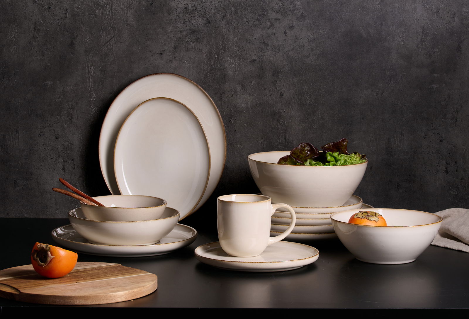 Ritzenhoff & Breker Schale OLIVIA Beige Geschirrset mit Schalen, Tellern und Tasse auf schwarzem Tisch vor dunklem Hintergrund, seitliche Perspektive.