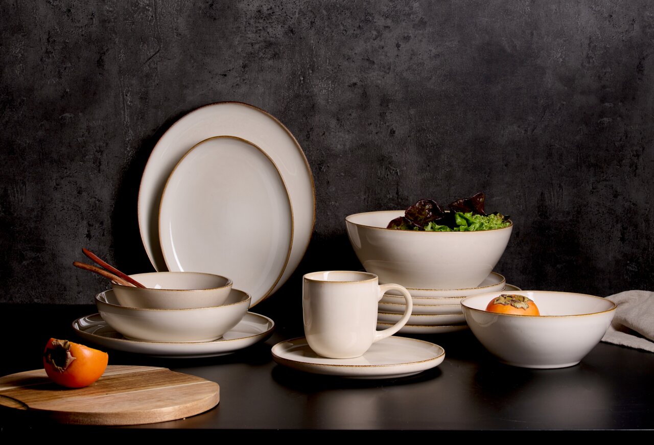 Ritzenhoff & Breker Schale OLIVIA Beige Geschirrset mit Schalen, Tellern und Tasse auf schwarzem Tisch vor dunklem Hintergrund, seitliche Perspektive.