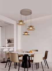 Drie moderne hanglampen met amberkleurige glazen schijven en warm licht boven een eettafel, gezien vanuit een schuin vooraanzicht van onderen.