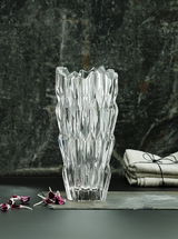Kristallvase mit facettiertem Design, frontal fotografiert, auf einem dunklen Hintergrund mit dekorativen Elementen.