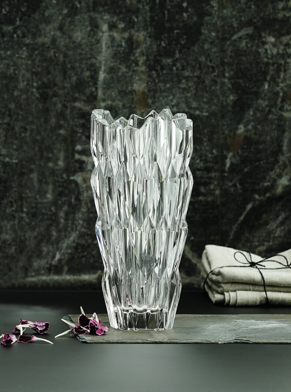 Kristallvase mit facettiertem Design, frontal fotografiert, auf einem dunklen Hintergrund mit dekorativen Elementen.