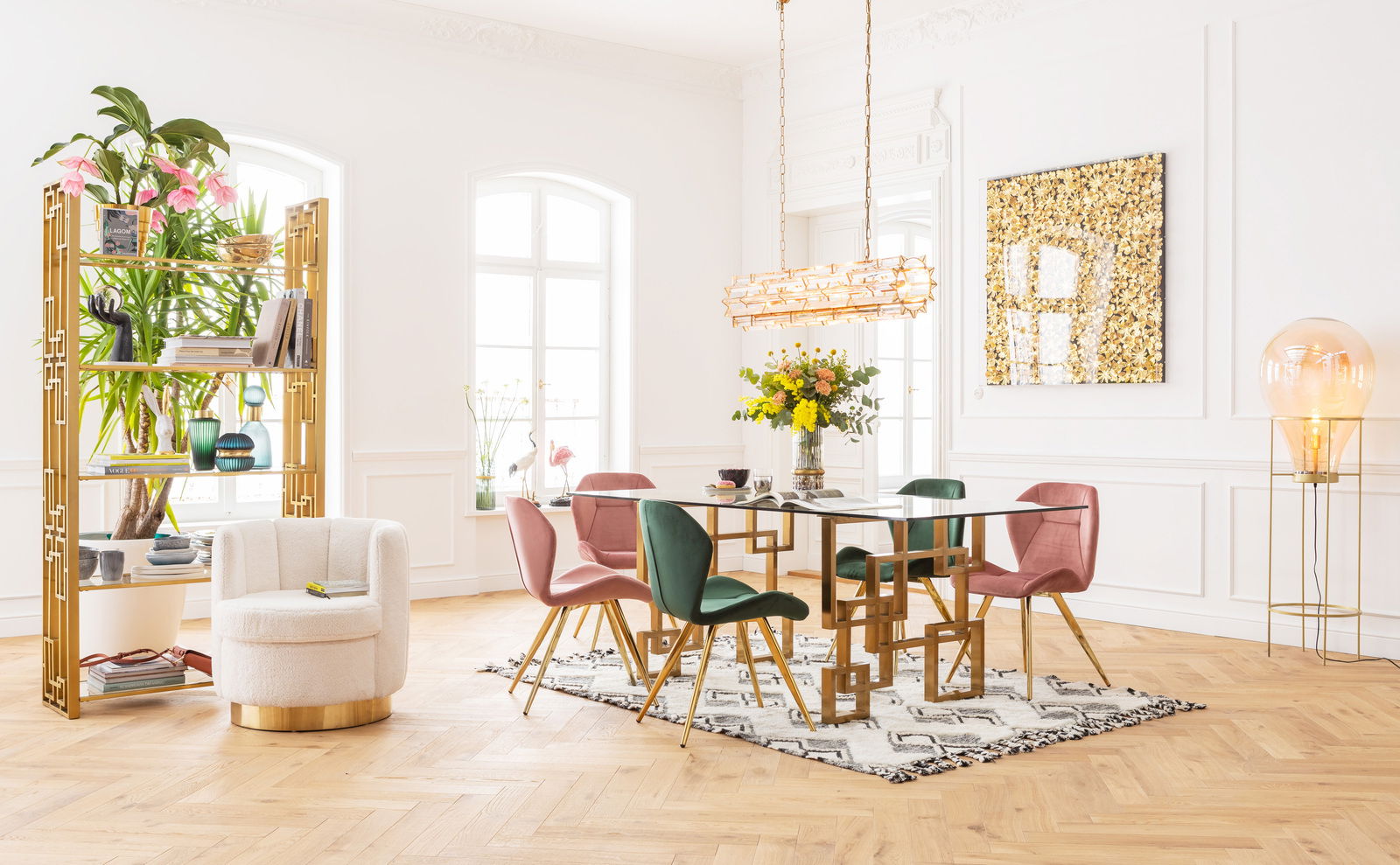 Esszimmer mit modernem Design: Ein eleganter Tisch mit goldenen Beinen und Glasplatte, umgeben von grünen und rosa Stühlen. Perspektive von vorne.
