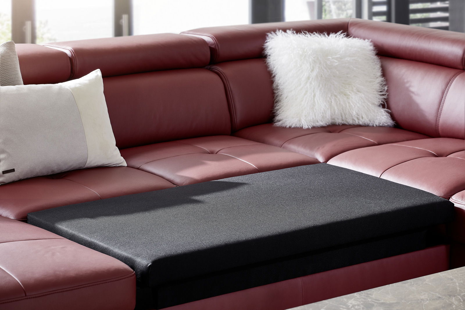 Rote Polsterrundecke mit schwarzen Kissen in einer modernen Wohnzimmerumgebung, seitliche Perspektive