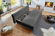 Graues Funktionssofa in einem modernen Wohnzimmer, von oben betrachtet, mit ausgeklappter Liegefläche, umgeben von Pflanzen, einem Kamin und einem Couchtisch.