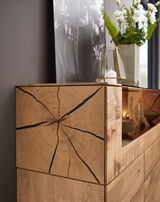 Nahaufnahme eines Sideboards aus Holz mit auffälliger Maserung und Rissen, dekoriert mit einer Vase und Kerze, seitliche Perspektive.