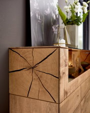 Close-up van een houten dressoir met opvallende nerf en scheuren, versierd met een vaas en een kaars, gezien vanuit de zijkant.