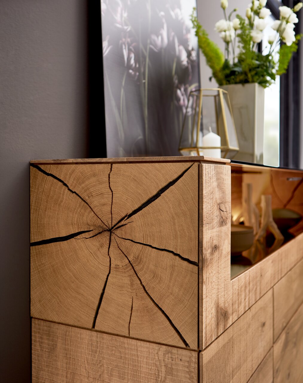 Close-up van een houten dressoir met opvallende nerf en scheuren, versierd met een vaas en een kaars, gezien vanuit de zijkant.