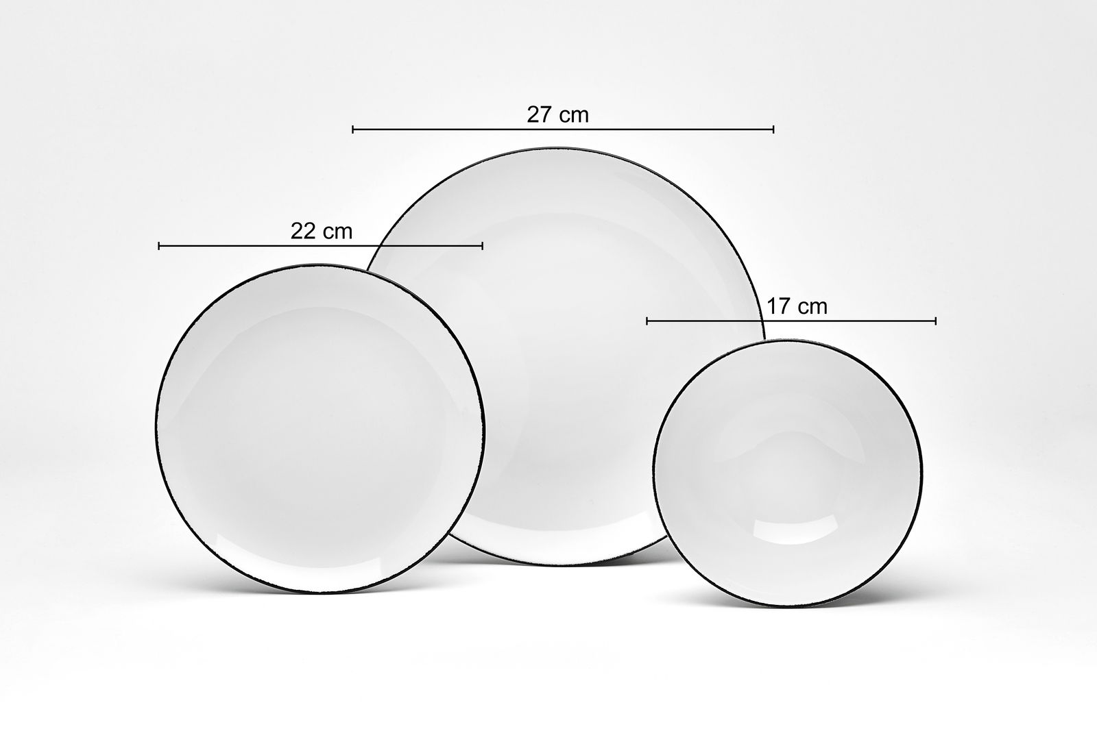 Drei weiße Teller mit schwarzem Rand in verschiedenen Größen (27 cm, 22 cm, 17 cm) aus der Vogelperspektive fotografiert.