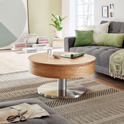 Moderner Couchtisch aus Holz mit runder Tischplatte und Metallfuß, in einem gemütlichen Wohnzimmer mit grauem Sofa und grünen Kissen, seitliche Perspektive.
