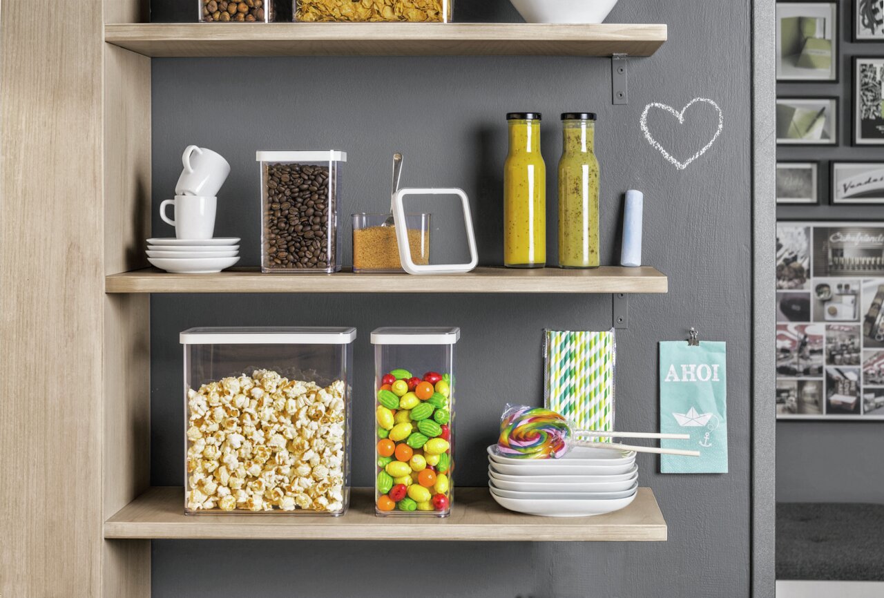 rotho Set voorraadbussen, 5-delig LOFT Loft-set van 5 voorraadbussen op een plank, gevuld met popcorn, koffiebonen en kleurrijke snoepjes, gefotografeerd vanuit een zijaanzicht.