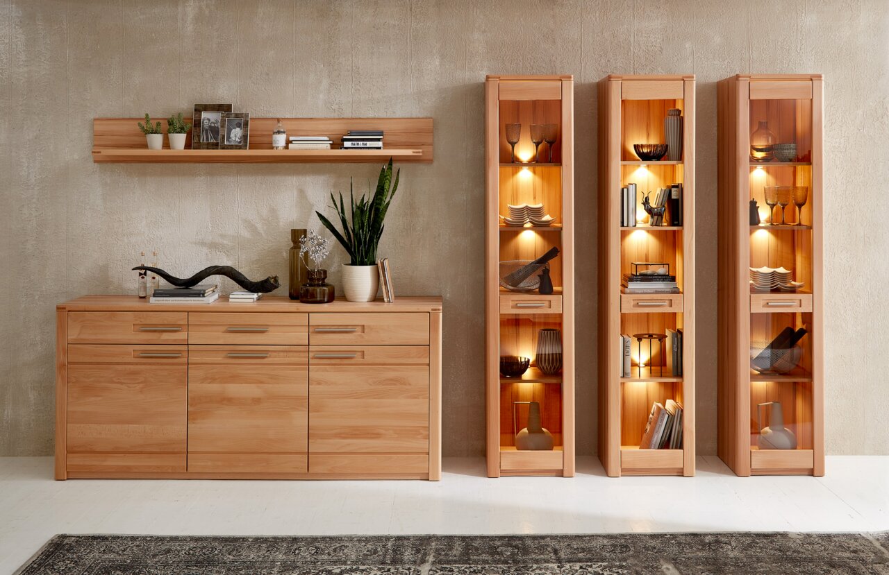 Schmale Vitrine aus Holz mit Glasfronten, beleuchtet, gefüllt mit dekorativen Objekten, aus frontaler Perspektive.