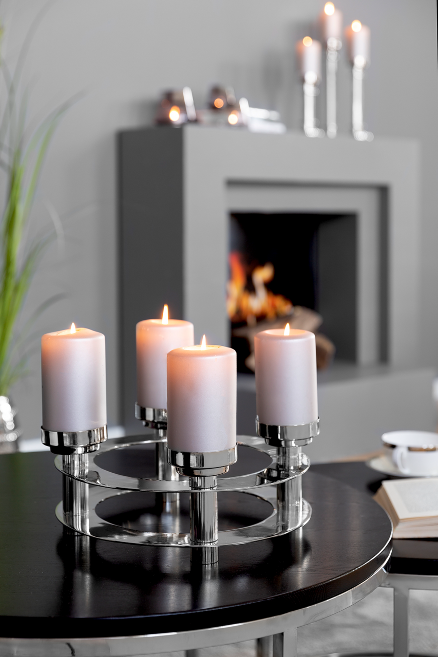 Moderner vierflammiger Kerzenhalter aus Metall mit brennenden Kerzen, auf einem Tisch in einem stilvollen Wohnzimmer platziert, seitliche Perspektive.