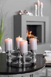 Moderner vierflammiger Kerzenhalter aus Metall mit brennenden Kerzen, auf einem Tisch in einem stilvollen Wohnzimmer platziert, seitliche Perspektive.