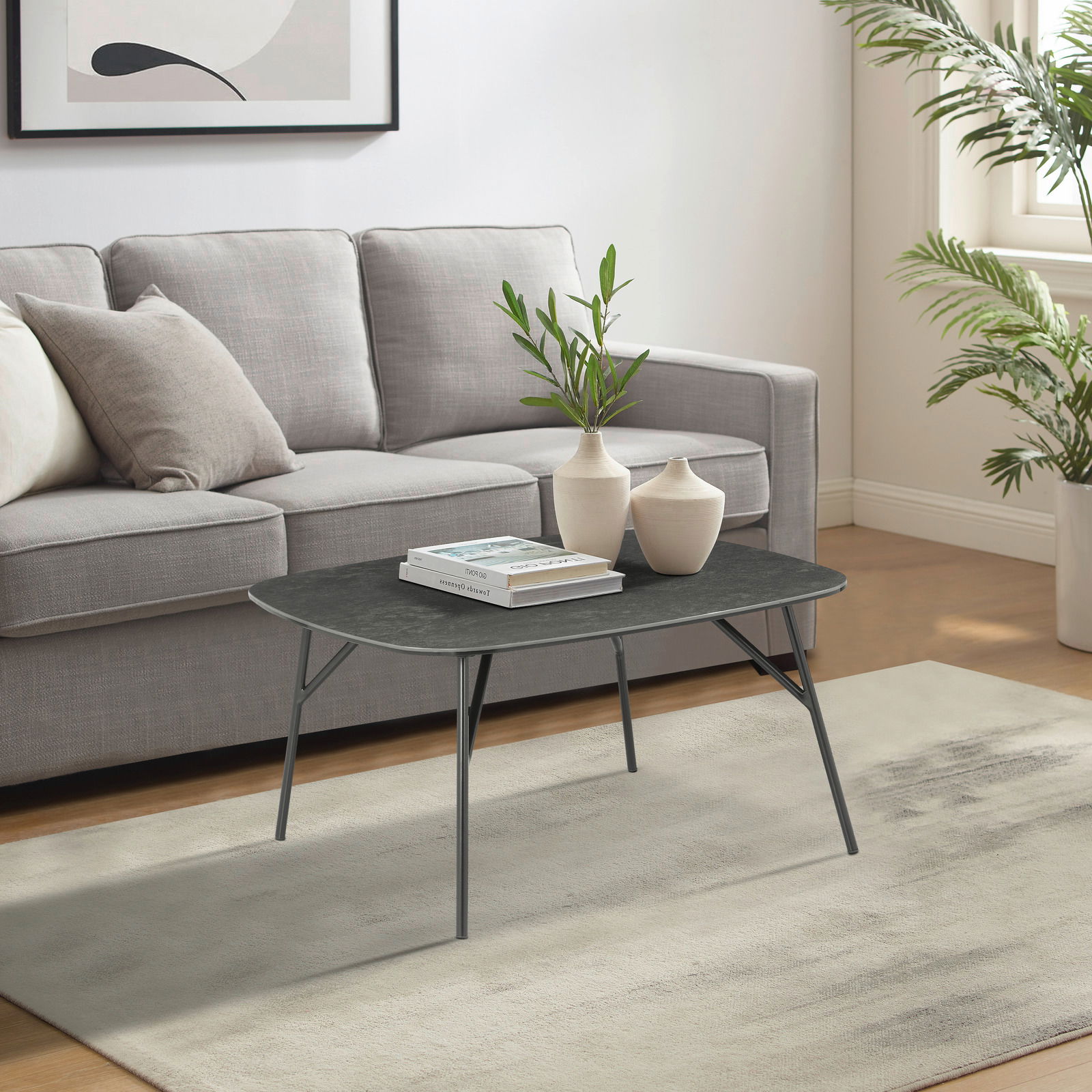 Moderner Couchtisch mit dunkler Tischplatte und schlanken Beinen, im Wohnzimmer vor einem grauen Sofa, seitliche Perspektive