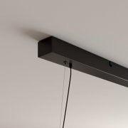 Schwarze, rechteckige Deckenhalterung einer Pendelleuchte mit sichtbarem Kabel und Abhängung, fotografiert aus schräger Untersicht.