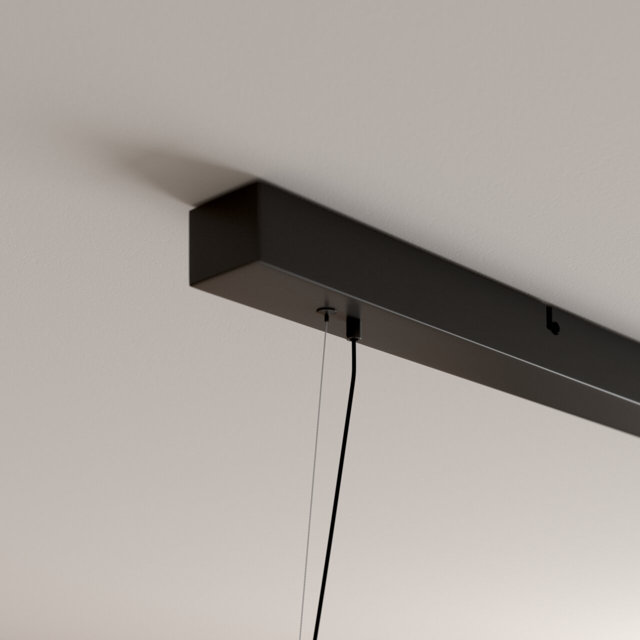 Zwarte, rechthoekige plafondbevestiging van een hanglamp met zichtbare kabel en ophanging, gefotografeerd vanuit een schuin onderaanzicht.