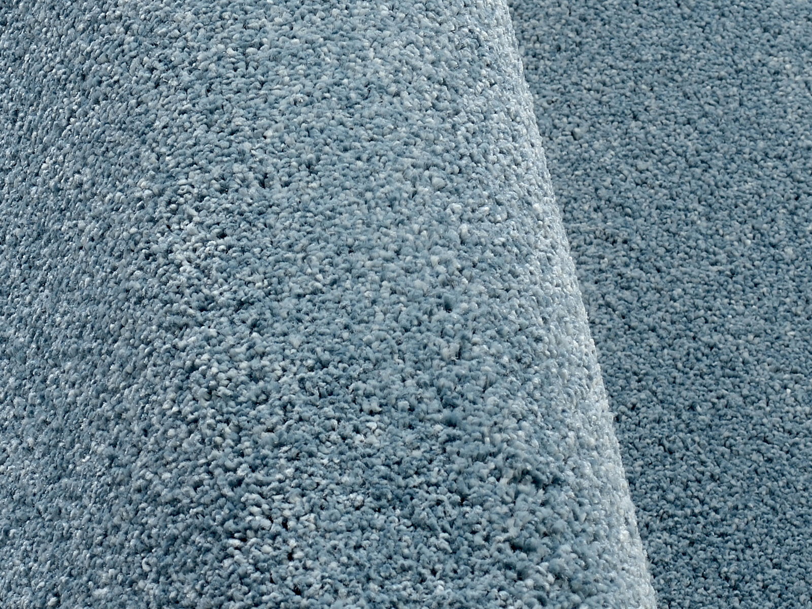 Nahaufnahme eines blauen Uni-Teppichs mit weicher, flauschiger Textur, seitliche Perspektive