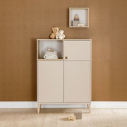 Beigefarbenes Highboard mit zwei Türen und einem offenen Fach, dekoriert mit Stofftieren und Babyzubehör, frontal fotografiert.