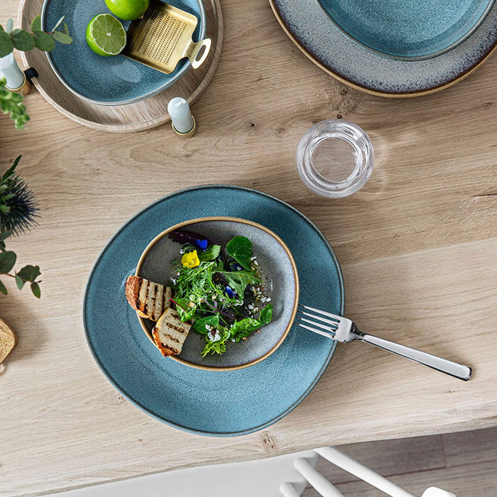 Like by Villeroy & Boch Schale flach LAVE BEIGE Vogelperspektive auf einen gedeckten Tisch mit einer Obstschale Lave 470ml beige, gefüllt mit Salat und gegrilltem Brot, umgeben von weiteren Tellern und Besteck.