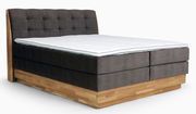 Boxspringbett mit grauem, gepolstertem Kopfteil und Holzrahmen, seitliche Perspektive