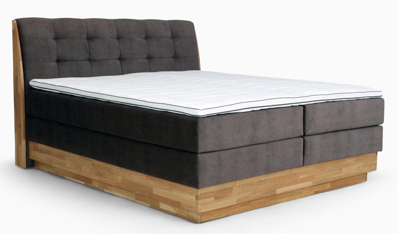 Boxspringbett mit grauem, gepolstertem Kopfteil und Holzrahmen, seitliche Perspektive