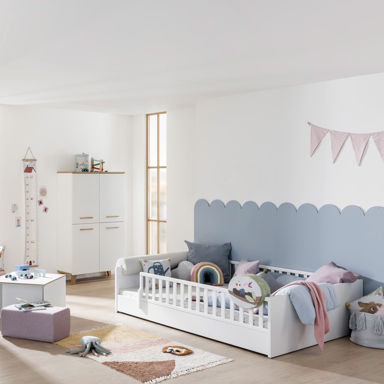 Kinderzimmer mit weißem Bodenbett und Rausfallschutz, dekoriert mit bunten Kissen und Decken, seitliche Perspektive