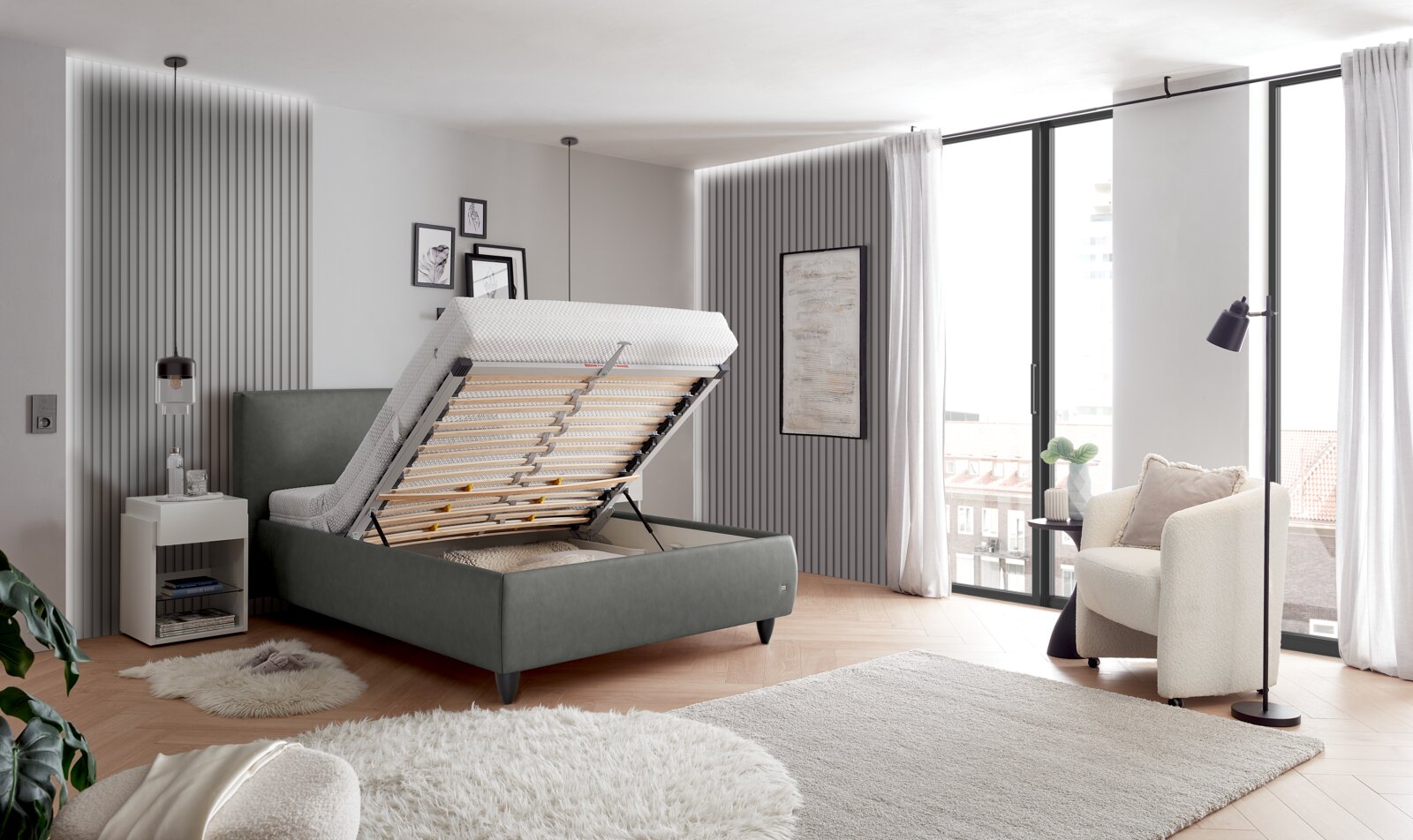Modernes graues Polsterbett mit hochgeklapptem Lattenrost und Stauraumkasten im Schlafzimmer, perspektivische Ansicht von schräg vorne links