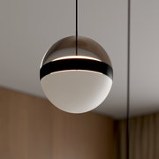 Moderne kugelförmige Pendelleuchte mit halbtransparentem braun getöntem Schirm, schwarzem Ring und weißem Diffusor, warm leuchtend, Nahaufnahme in leichter Untersicht
