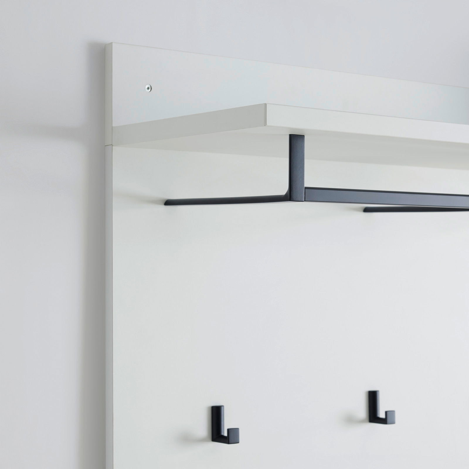 Garderobenpaneel in seitlicher Perspektive mit weißem Regalbrett und schwarzen Haken.