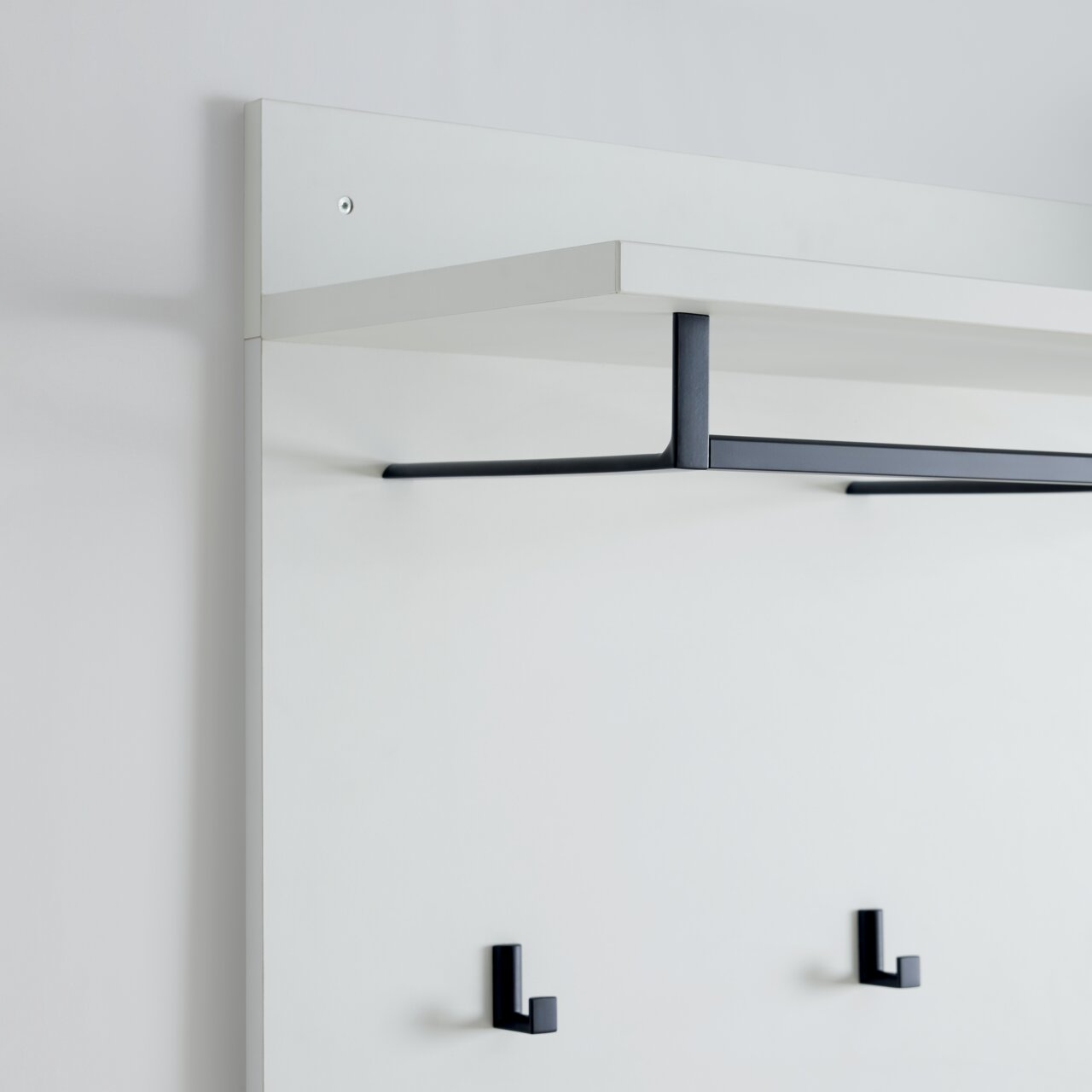 Garderobenpaneel in seitlicher Perspektive mit weißem Regalbrett und schwarzen Haken.