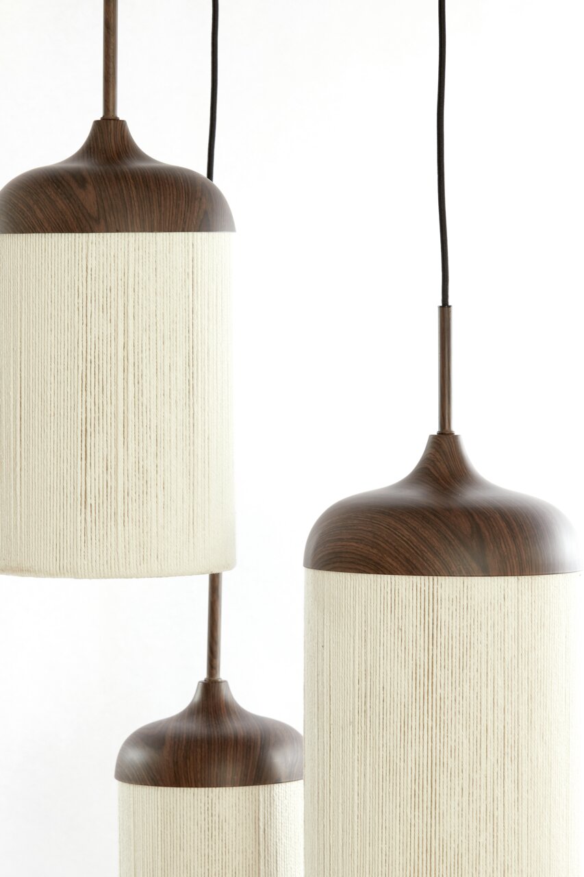 Drie moderne hanglampen met een donkerbruine houtlook en een cilindervormige, crèmekleurige stoffen kap, hangend tegen een witte achtergrond close-up vanuit een licht zijdelings perspectief