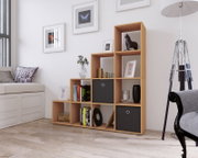 Modernes, asymmetrisches Würfelregal aus hellem Holz mit schwarzen Stoffboxen, dekoriert mit Büchern und Vasen, in einem hellen Wohnzimmer; Perspektive: frontale Ansicht leicht von links.