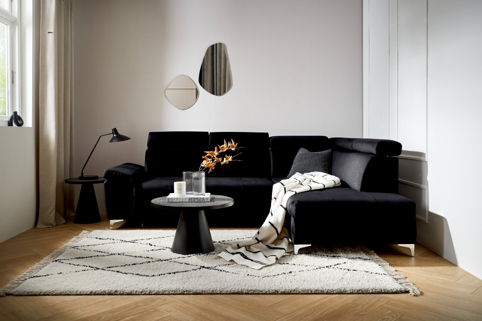 Zwarte hoekbank (L) in een moderne woonkamer, zijaanzicht, met een bijzettafeltje en decoraties.