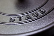 Nahaufnahme des Deckels eines runden Bräters der Marke Staub, mit Fokus auf das eingeprägte Logo.
