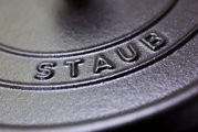 Close-up van het deksel van een ronde braadpan van het merk Staub, met de nadruk op het ingeperste logo.