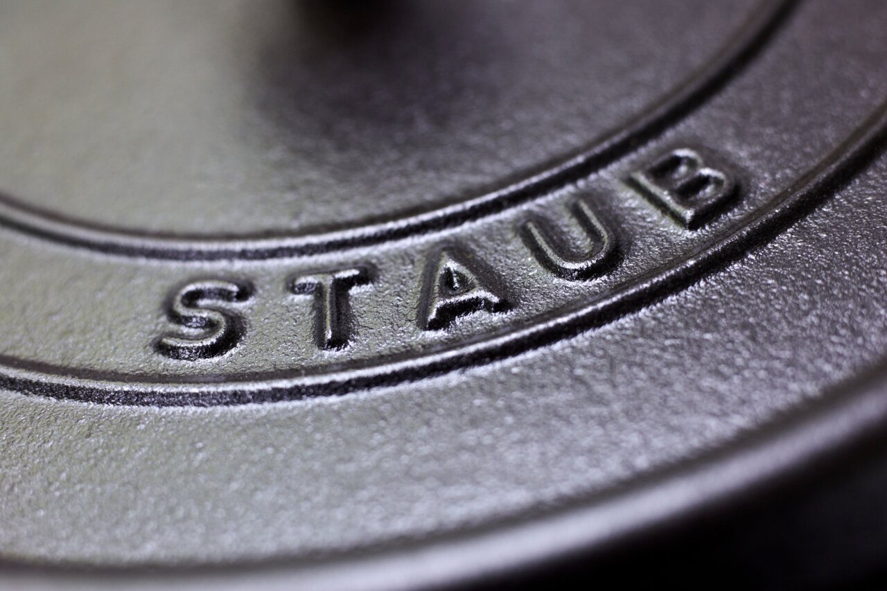 Close-up van het deksel van een ronde braadpan van het merk Staub, met de nadruk op het ingeperste logo.