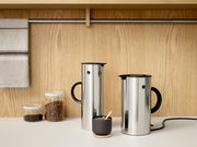 Zwei elegante Isolierkannen aus Stahl mit schwarzem Griff, auf einer Küchenarbeitsplatte vor einer Holzwand, aus seitlicher Perspektive fotografiert.
