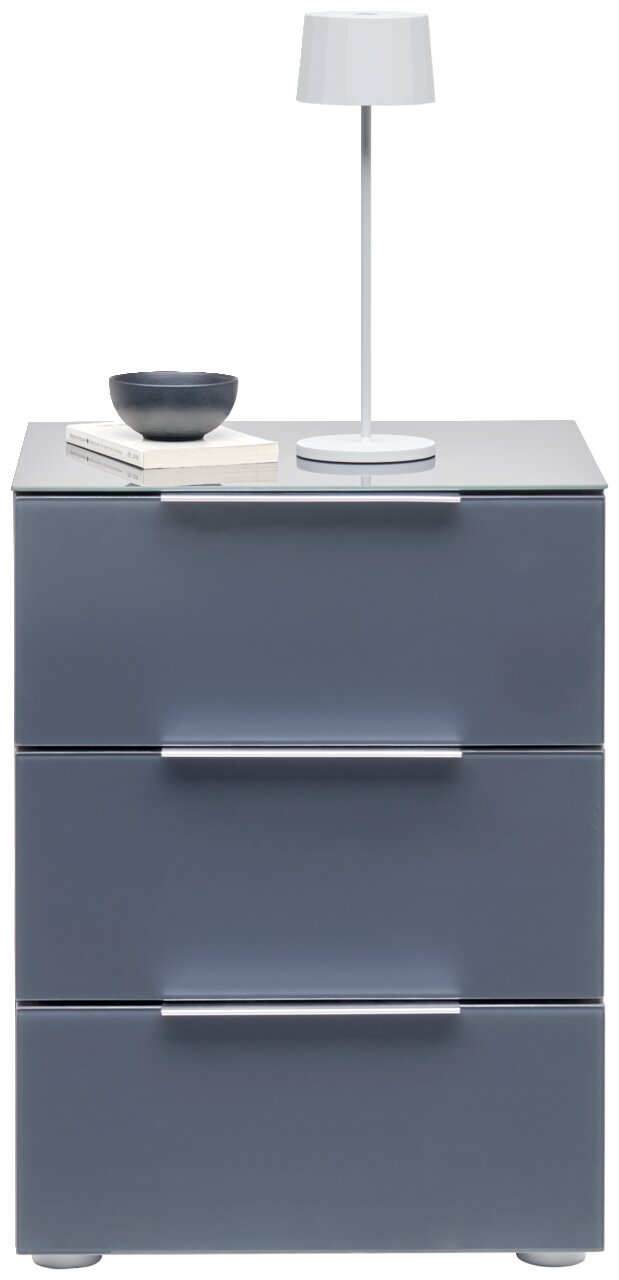 Moderne Nachtkonsole mit drei Schubladen in grauer Farbe, darauf eine weiße Tischlampe, eine Schale und Bücher. Frontalansicht.