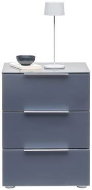 Moderne Nachtkonsole mit drei Schubladen in grauer Farbe, darauf eine weiße Tischlampe, eine Schale und Bücher. Frontalansicht.
